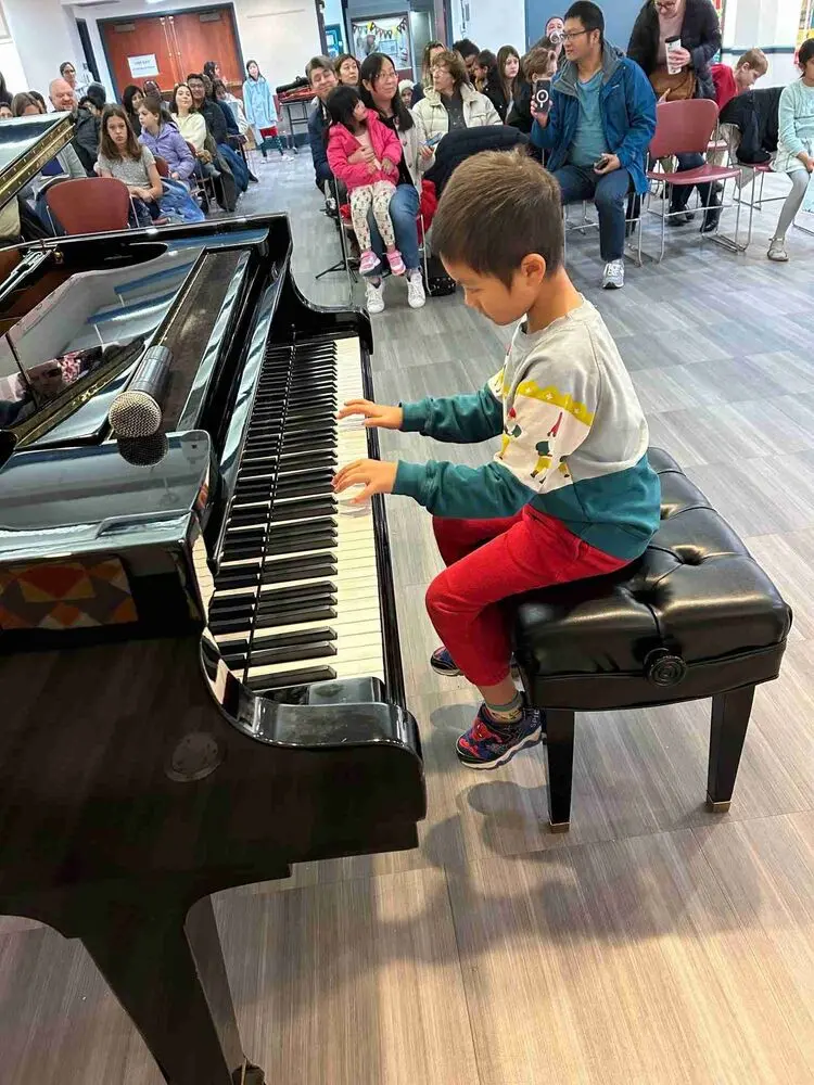 A young pianist dressed in a festive sweater delights the audience with his performance at the Allegro Music School Winter Recital.