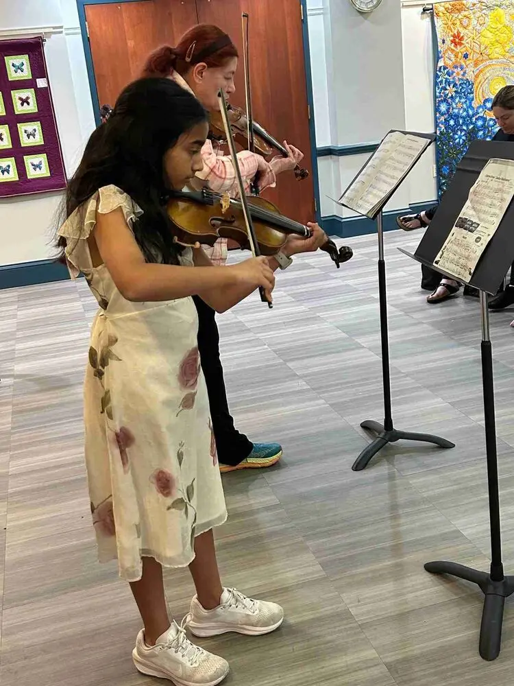 A talented young violinist in a floral dress performs beautifully at the Allegro Music School Winter Recital.