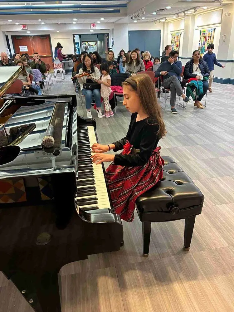 An Allegro Music School student performs a festive piano piece at the Winter Recital 2024, dressed in a charming outfit.