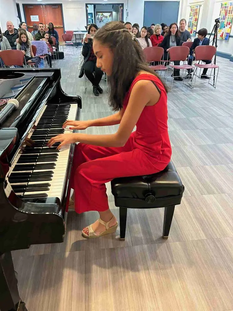 A young Allegro Music School pianist in a red jumpsuit captivates the audience during the Winter Recital 2024.